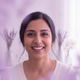A smiling South Asian woman in her late 30s, looking content and trustworthy, against a soft lavender and bright white backgr